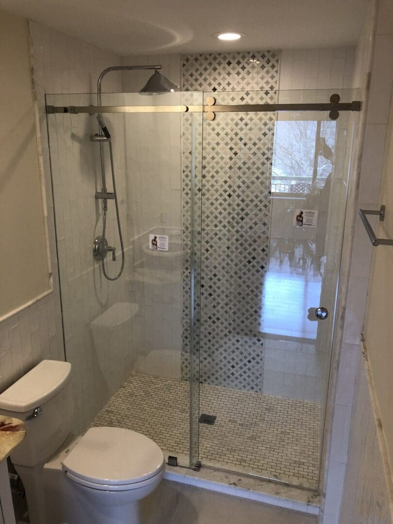 A bathroom with a glass shower door and tiled walls.